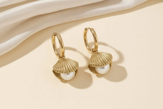 Gold shell earrings with pearl centers on a beige background, showing measurements.